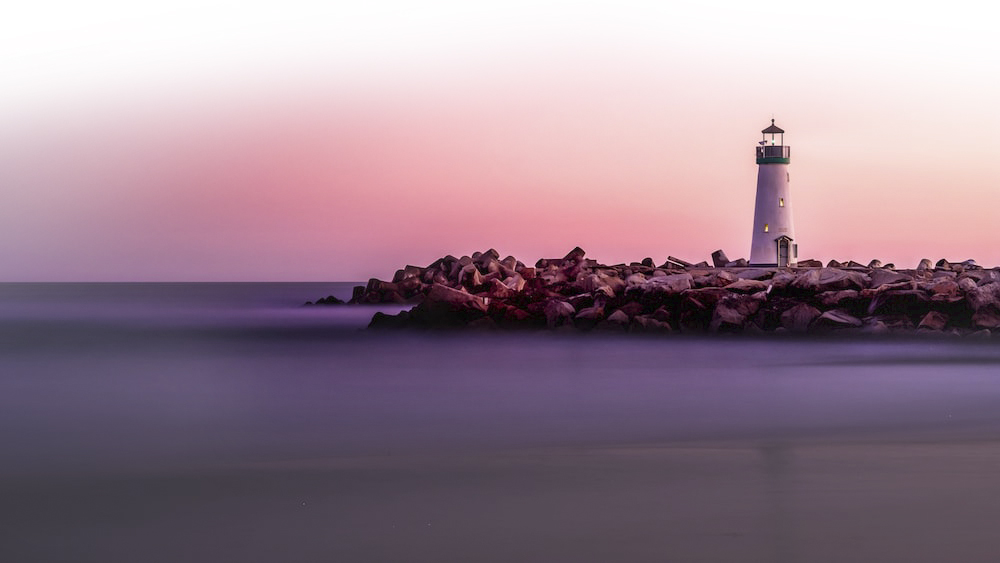 A calm image of a lighthouse against a blushing pink sky